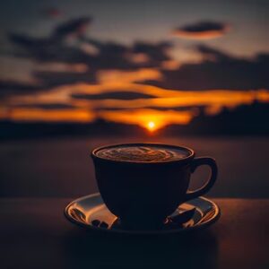 A coffee cup on a saucer, silhouetted against a vibrant sunset backdrop.