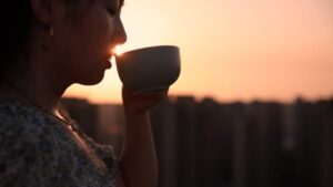 A woman enjoying a cup of coffee at sunrise, with the city skyline in the background.